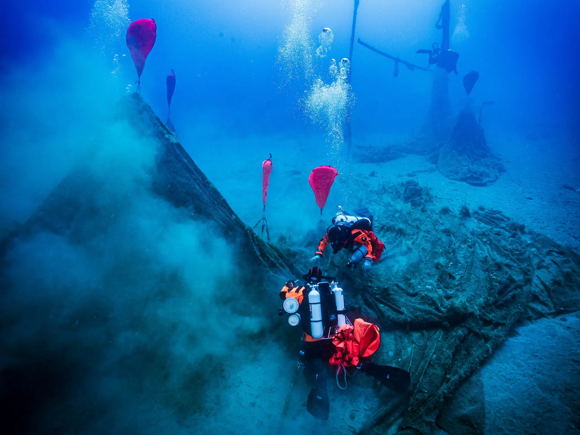 Two divers recovering an abandoned fishing net with lift bags in clear blue water
