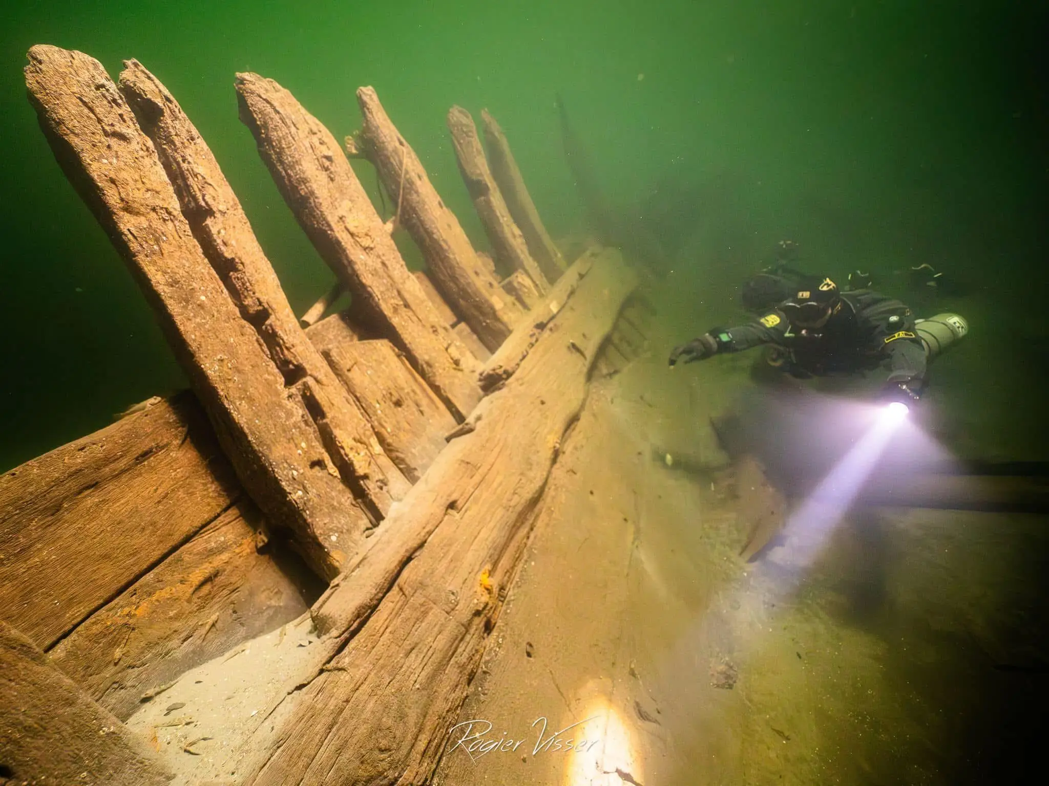Wooden shipwreck with upright ribs, a diver with a torch alongside
